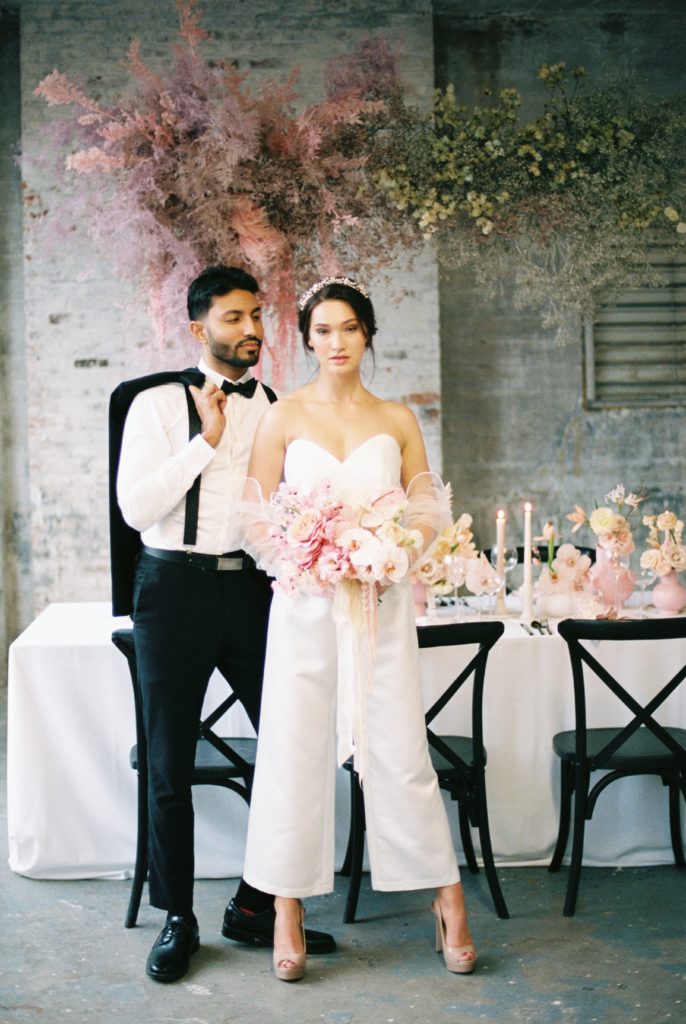 Couple standing poised next to wedding reception table 